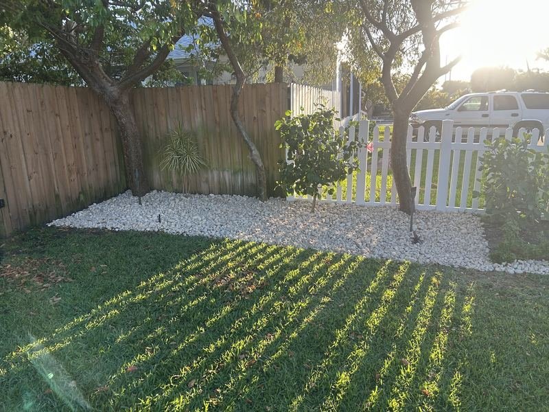 Finished landscape bed of white rock around trees against a fence line