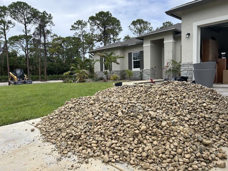 A load of tan river rock placed on a driveway beside the garage rather than at the street