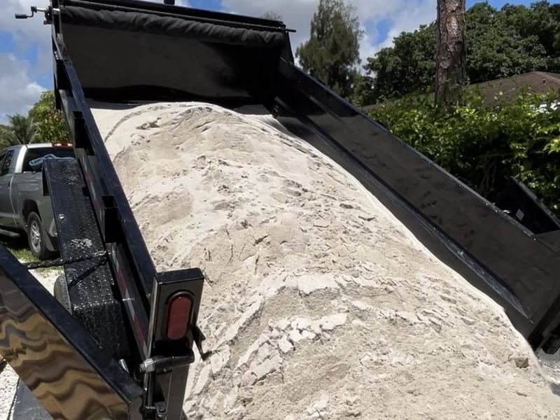 Dump trailer tipping a load of fill sand onto a tarp at a Palm Beach County property